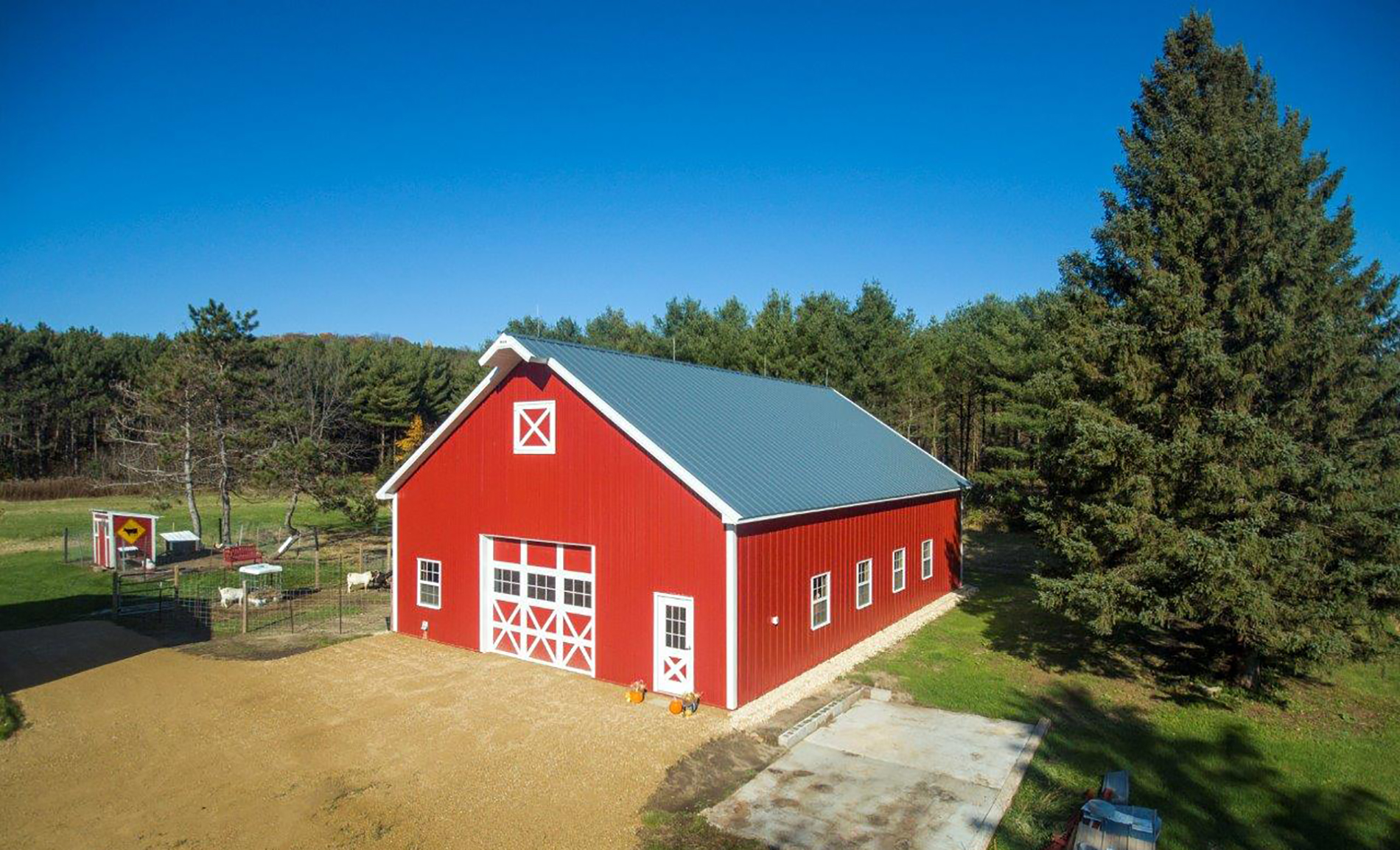 StewBer Buildings featured project: post frame agricultural animal confinement building; exterior featuring red siding with white trim with an adjacent outdoor goat pen